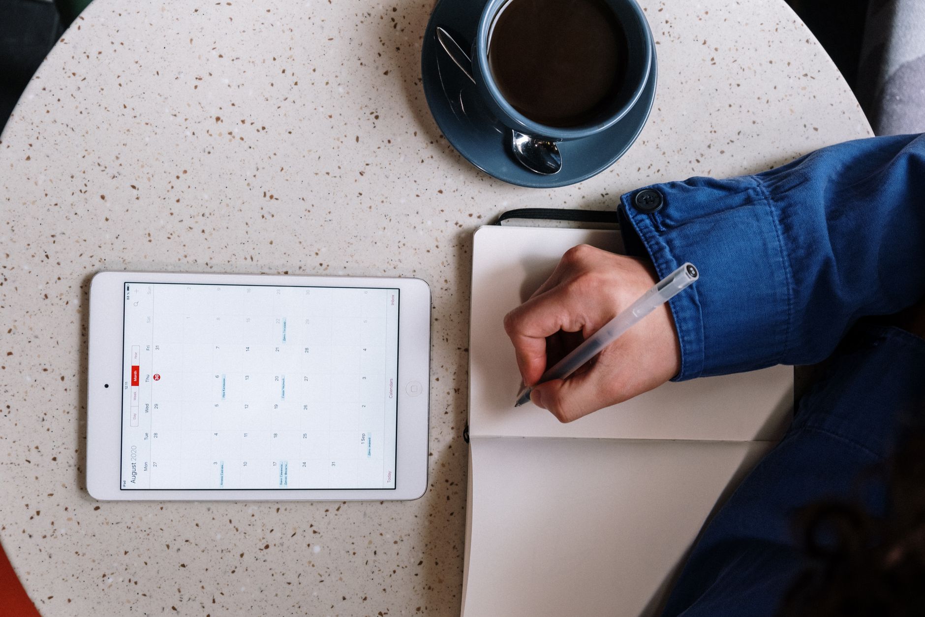 A person writes a daily schedule in a notebook while a smartphone shows an AI-generated plan.