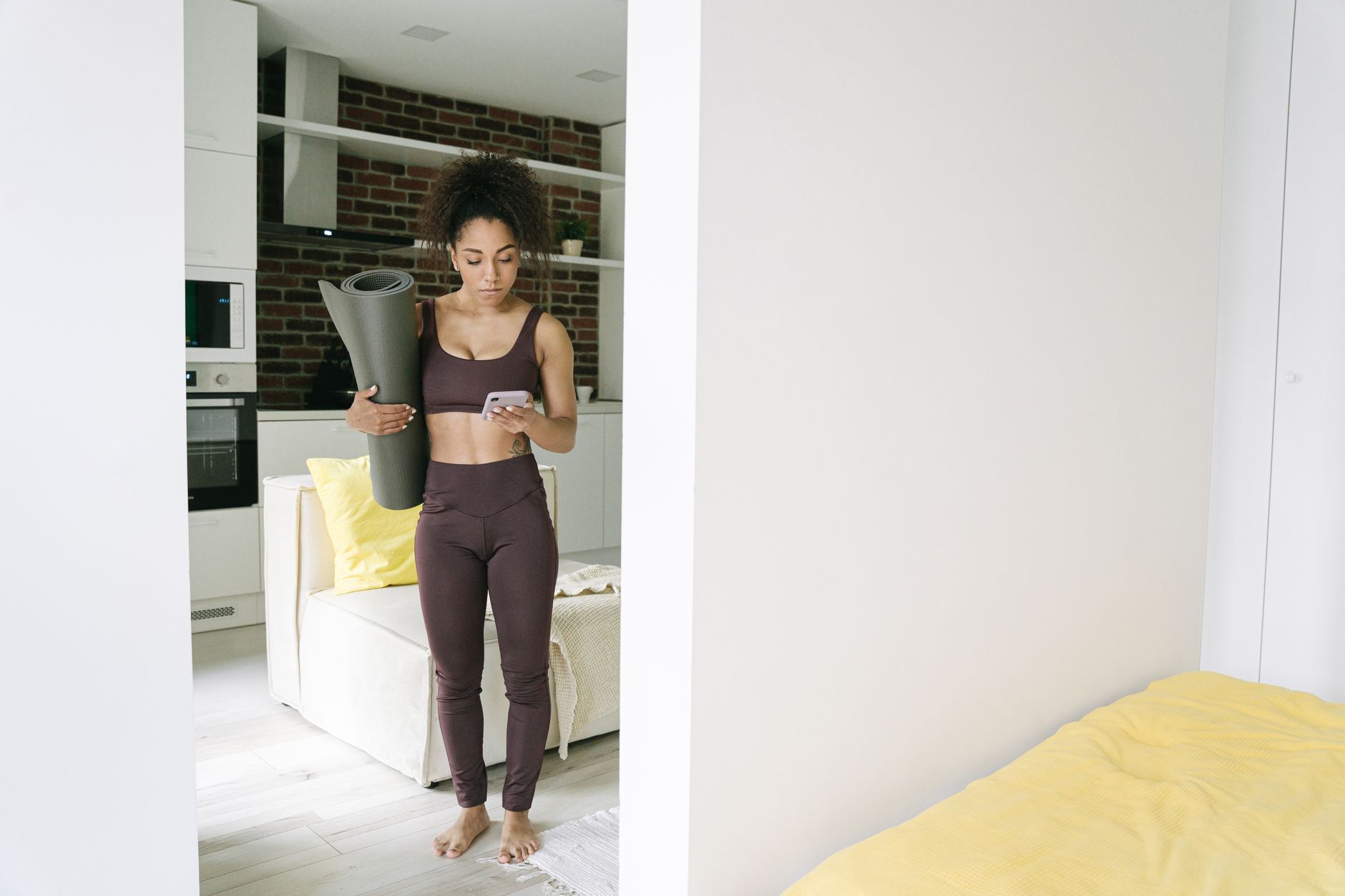 A woman holds a phone and checks exercise form while standing in a living room.