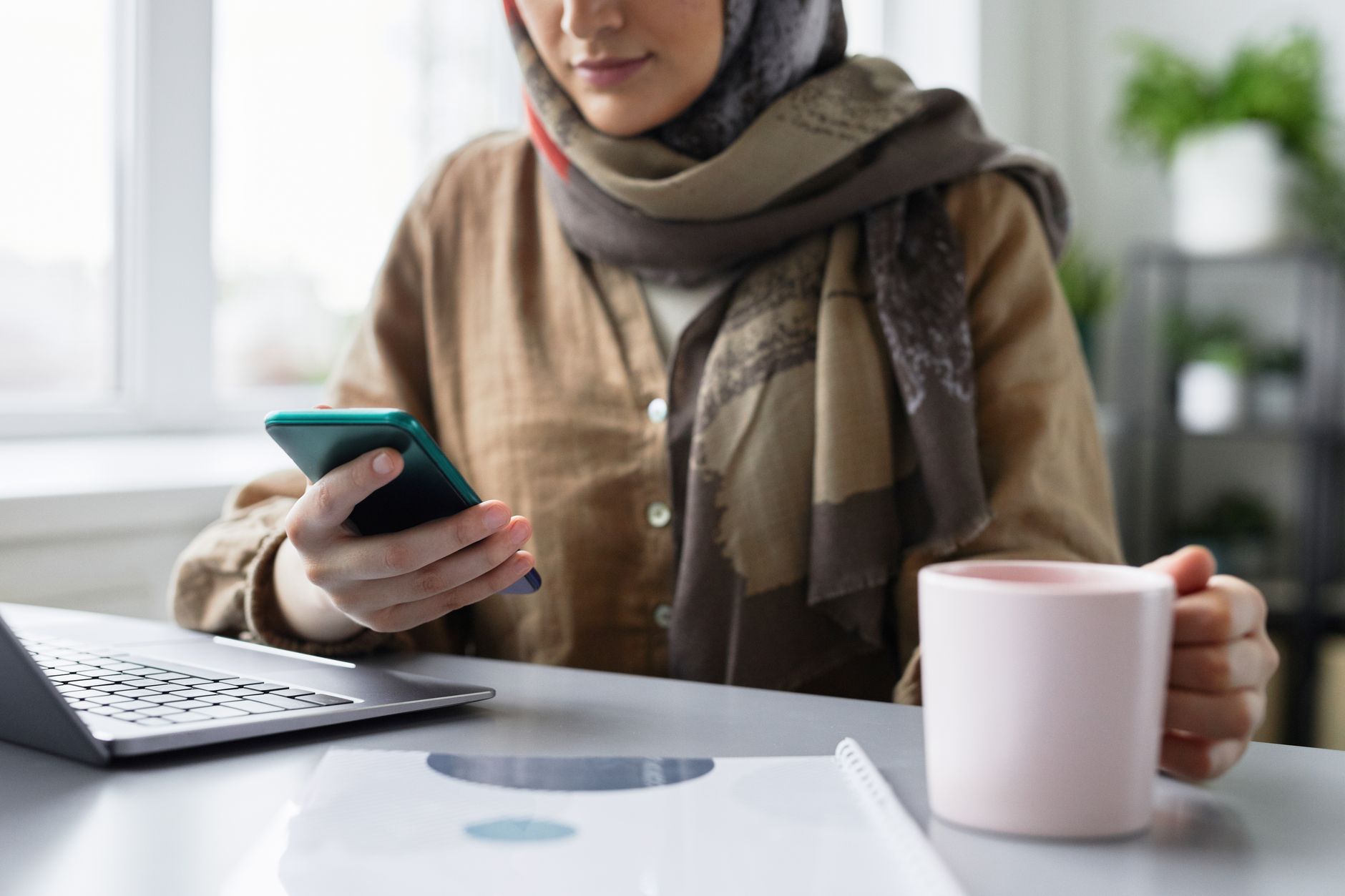A person comparing a caption draft on a phone with a laptop open at a home desk.