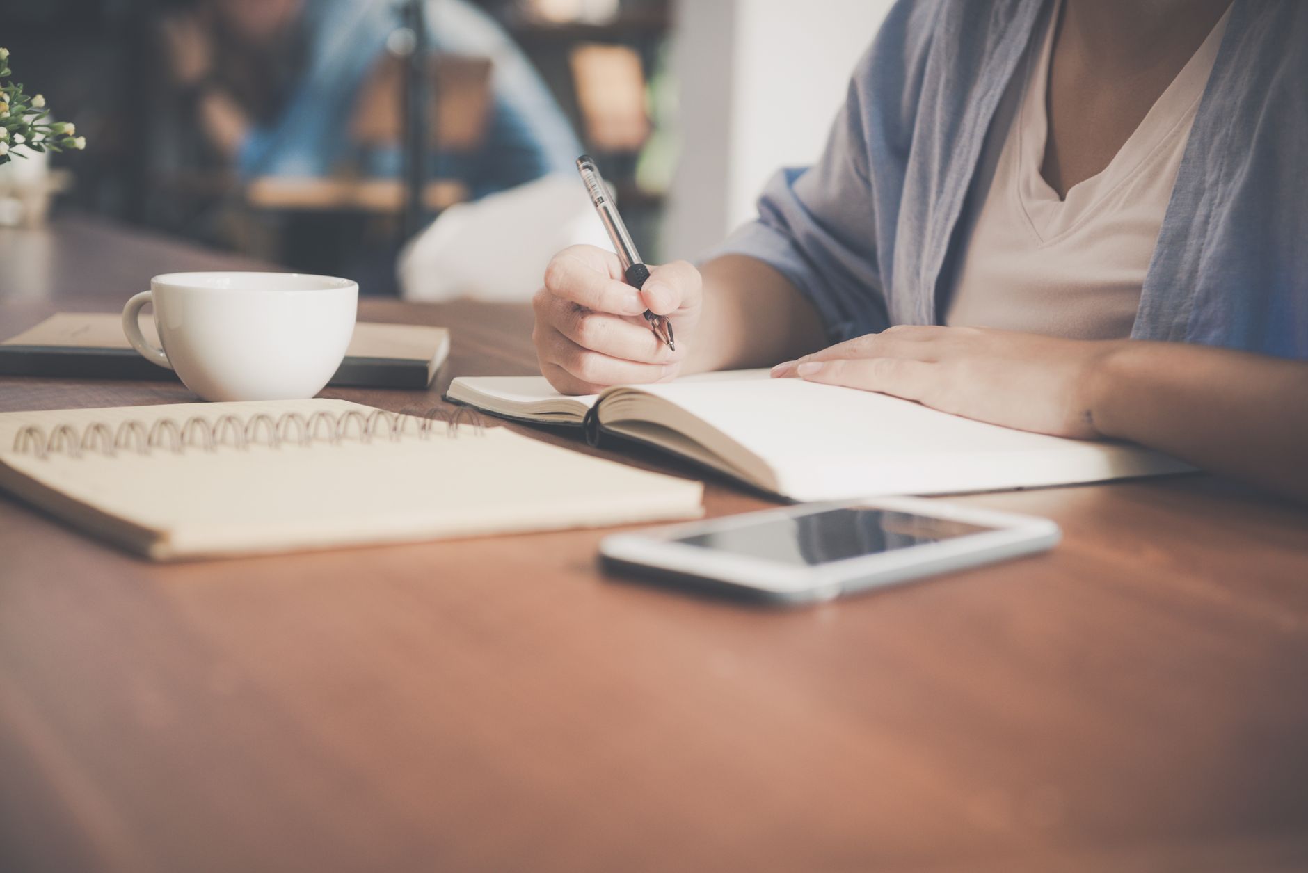 A student sits at a desk writing an essay with a notebook and coffee nearby.