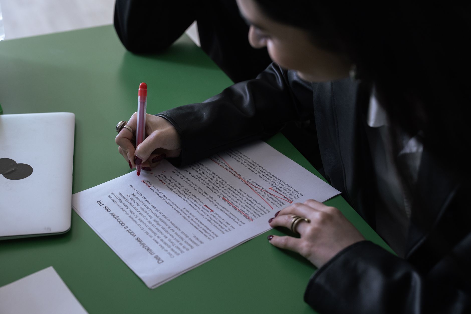 A person crosses out a sentence on paper with a red pen, showing careful editing.